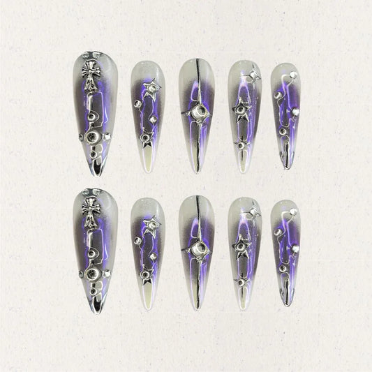 Celestial Radiance presents gradient silver and purple press-on nails with metallic embellishments, including stars and crosses, evoking a celestial and sophisticated style.