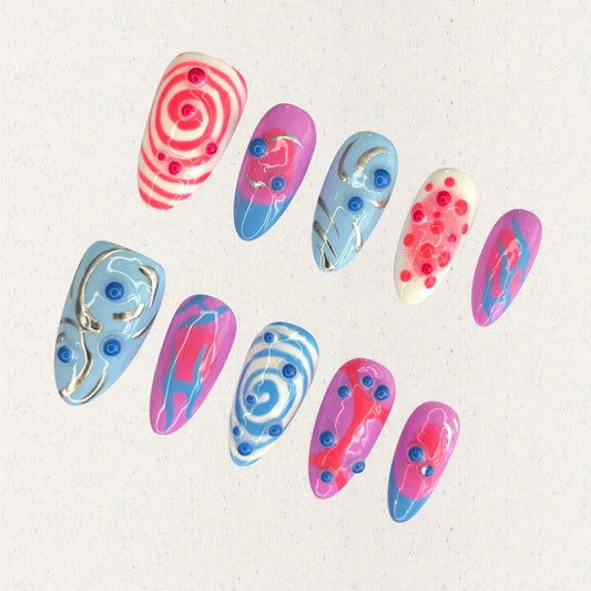 Cosmic Swirls nail set features bold swirls of pink, blue, and white, accented with metallic details and circular 3D elements. This playful yet elegant design mirrors the energetic flow of cosmic waves and nebulae.