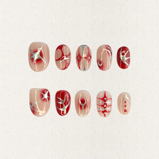 A press-on nail set featuring nude blush gradients with bold red patterns, celestial starbursts, and intricate white accents, creating an ethereal and romantic design.