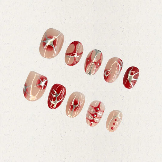 A press-on nail set featuring nude blush gradients with bold red patterns, celestial starbursts, and intricate white accents, creating an ethereal and romantic design.
