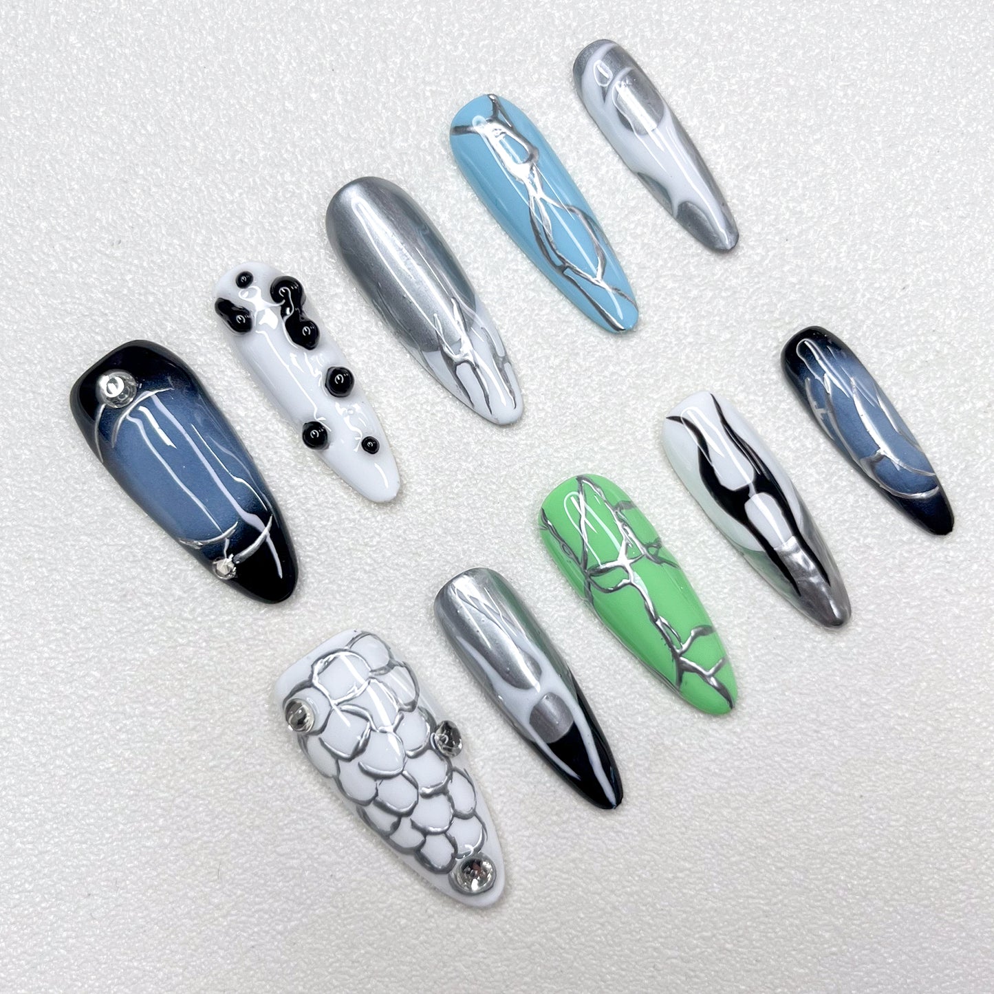 Press-on nails inspired by cyberpunk aesthetics, showcasing metallic silver veins across glossy black, green, blue, and white bases, accented with chrome details and geometric patterns for a bold techwear vibe.