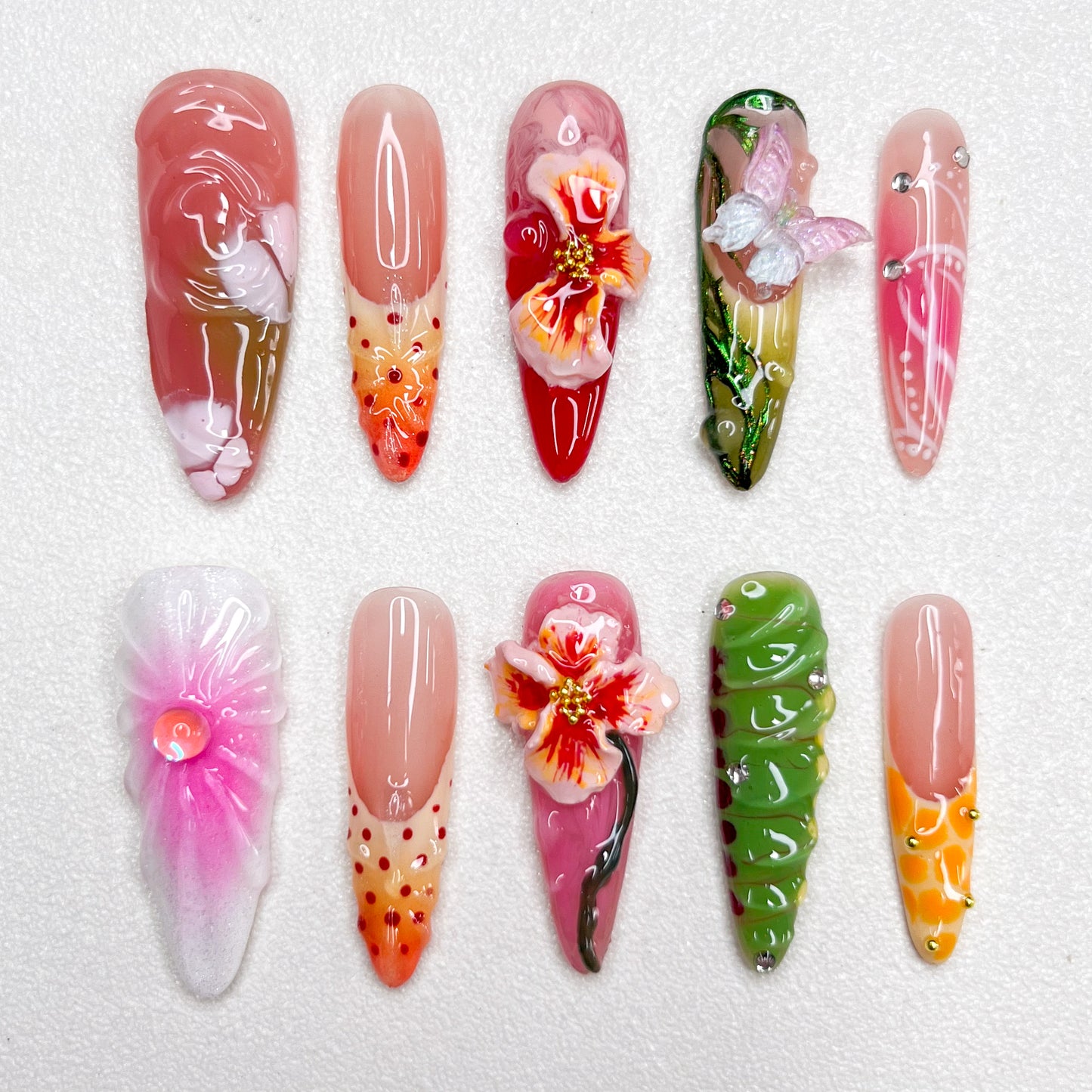 Colorful press-on nail set with tropical themes, showcasing 3D hibiscus flowers, butterflies, and floral gradients in pink, green, orange, and red, capturing a lush garden vibe.