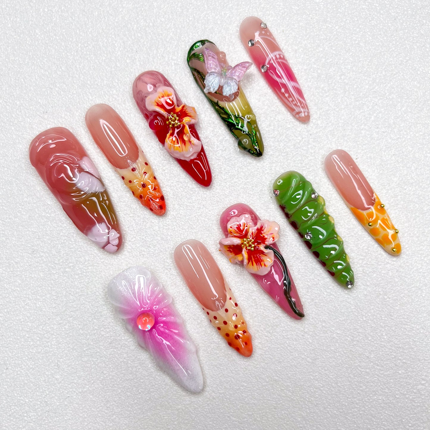 Colorful press-on nail set with tropical themes, showcasing 3D hibiscus flowers, butterflies, and floral gradients in pink, green, orange, and red, capturing a lush garden vibe.