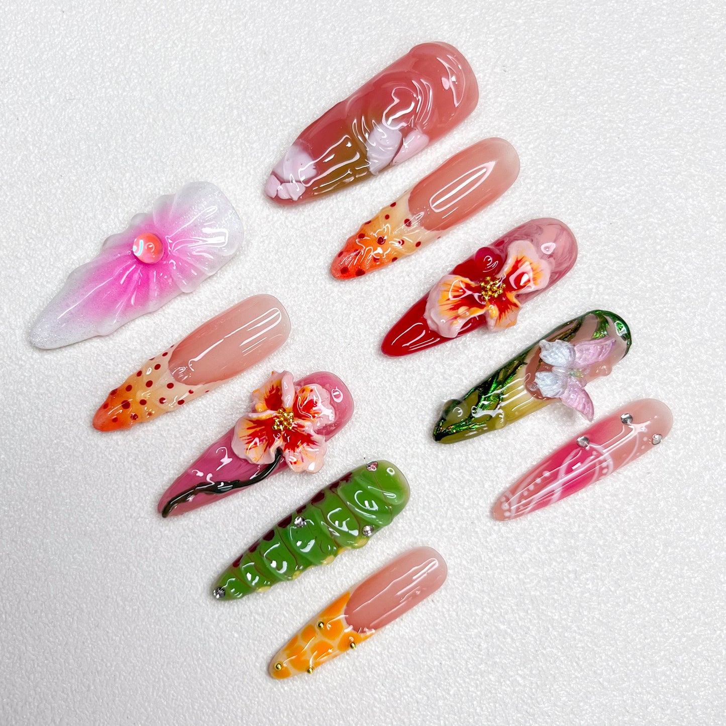 Colorful press-on nail set with tropical themes, showcasing 3D hibiscus flowers, butterflies, and floral gradients in pink, green, orange, and red, capturing a lush garden vibe.