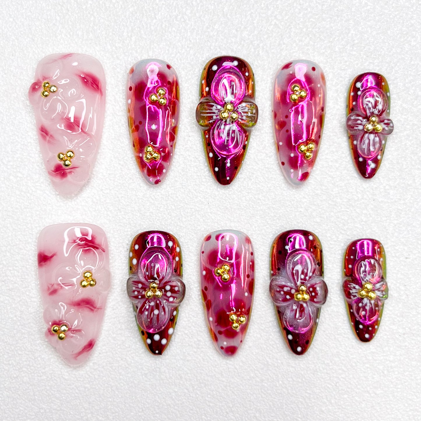 Glossy red and pink press-on nails with 3D flower details, golden bead centers, and shimmering gradient effects—elegant and bold for standout occasions.