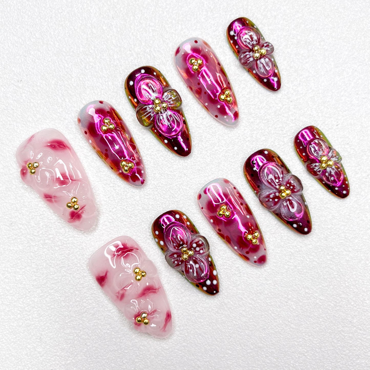Glossy red and pink press-on nails with 3D flower details, golden bead centers, and shimmering gradient effects—elegant and bold for standout occasions.