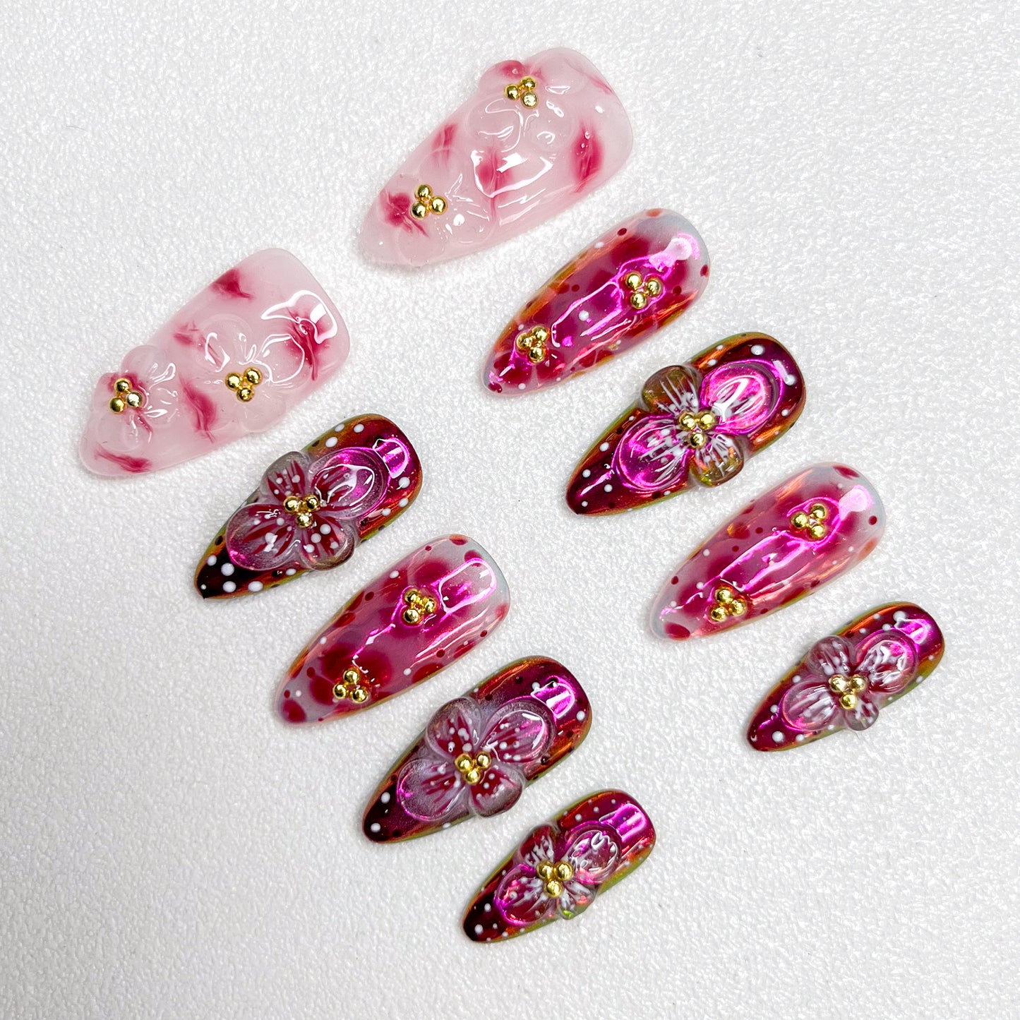 Glossy red and pink press-on nails with 3D flower details, golden bead centers, and shimmering gradient effects—elegant and bold for standout occasions.