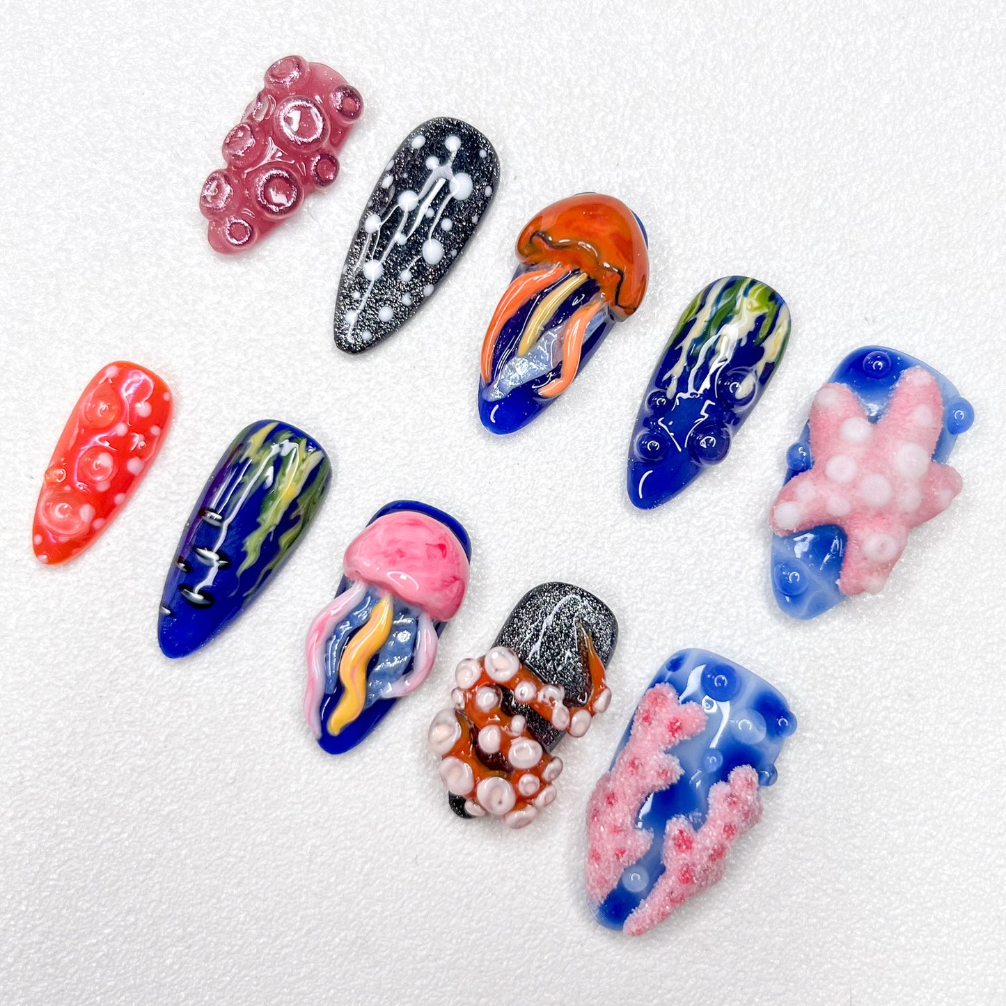 Hand-painted ocean-themed press-on nails with jellyfish, starfish, coral reef, and tentacle designs in deep blue, pink, and black tones—perfect for marine-inspired nail lovers.