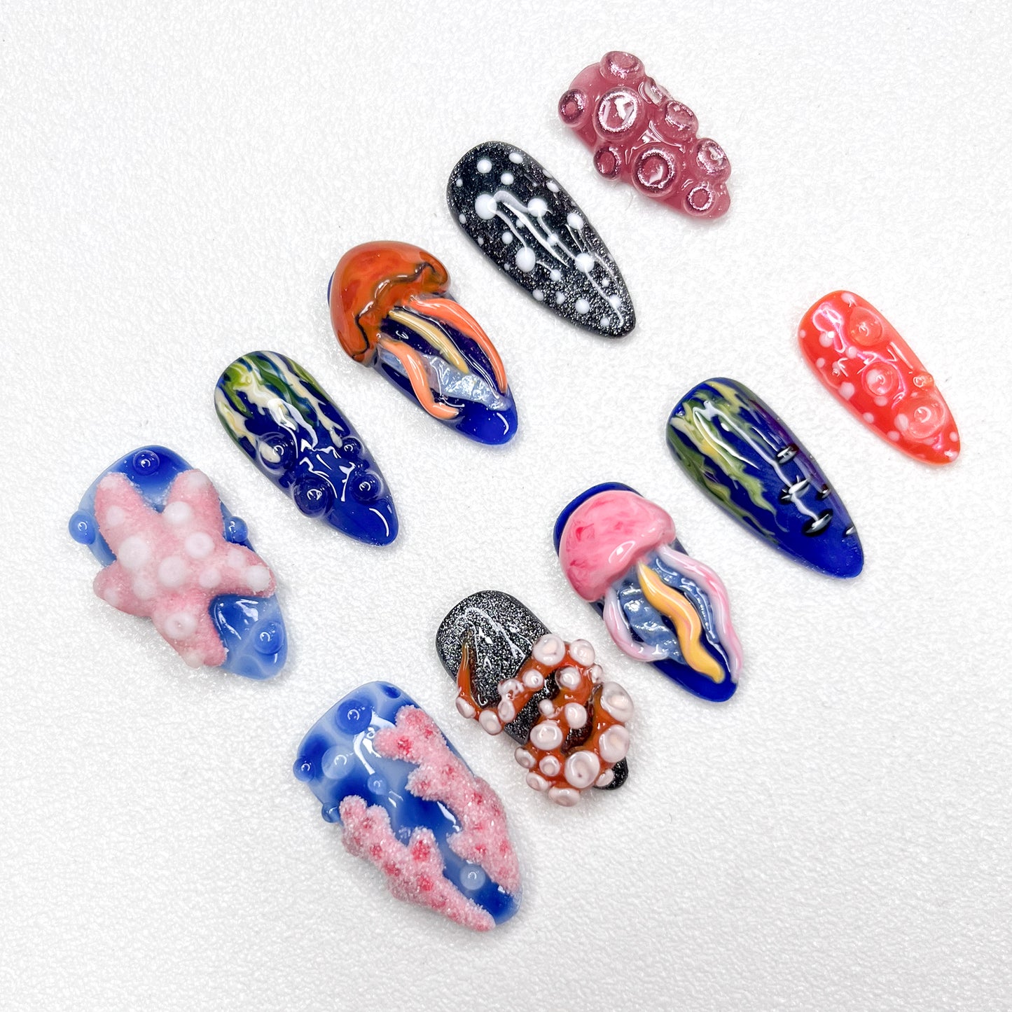 Hand-painted ocean-themed press-on nails with jellyfish, starfish, coral reef, and tentacle designs in deep blue, pink, and black tones—perfect for marine-inspired nail lovers.