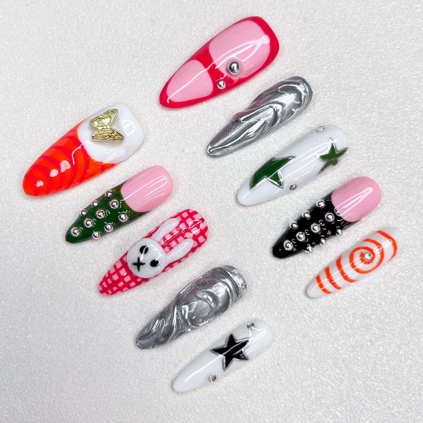 Colorful press-on nails with a mix of stars, spirals, plaid bunny patterns, chrome swirls, and metallic studs—fun, edgy, and fashion-forward Y2K-inspired designs.