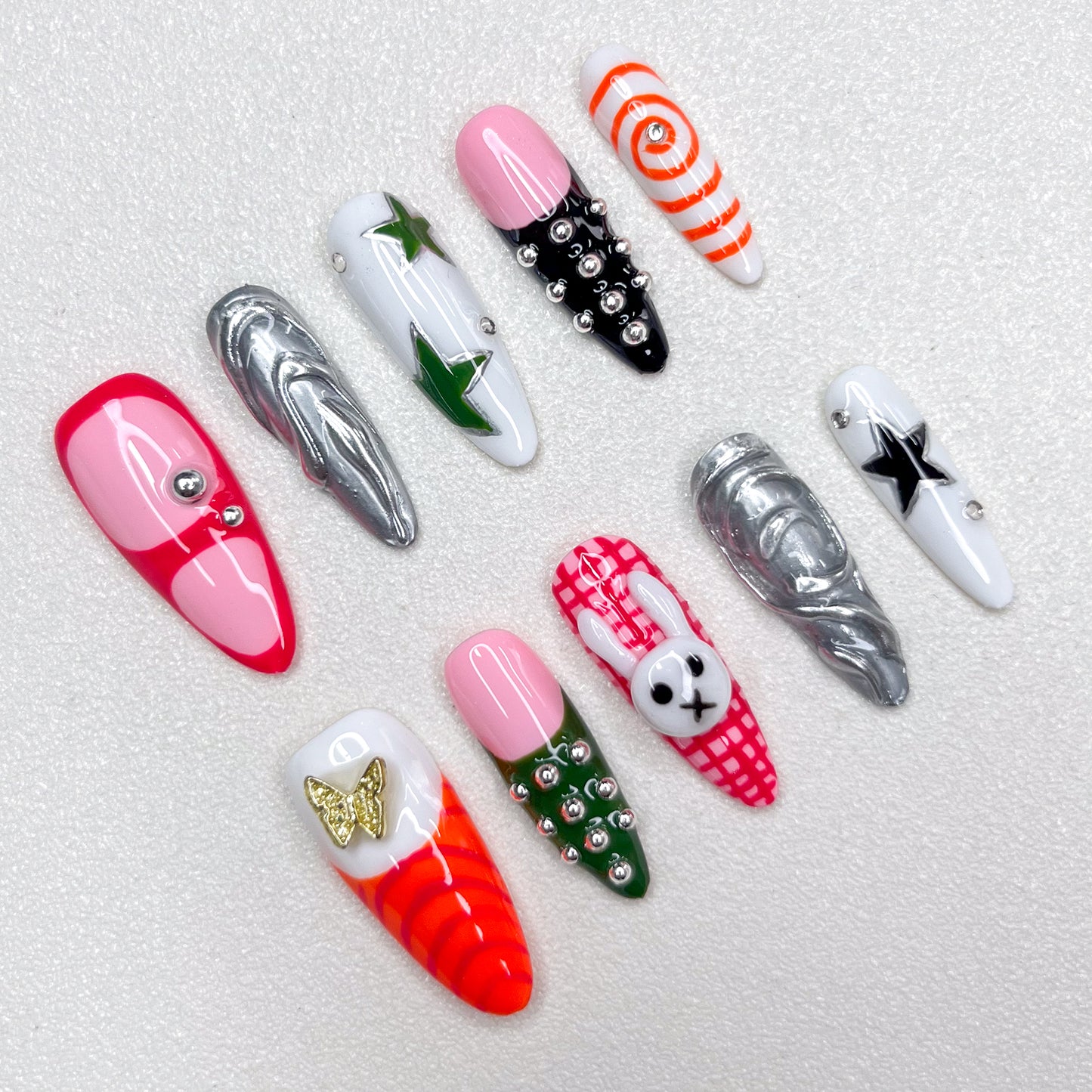 Colorful press-on nails with a mix of stars, spirals, plaid bunny patterns, chrome swirls, and metallic studs—fun, edgy, and fashion-forward Y2K-inspired designs.