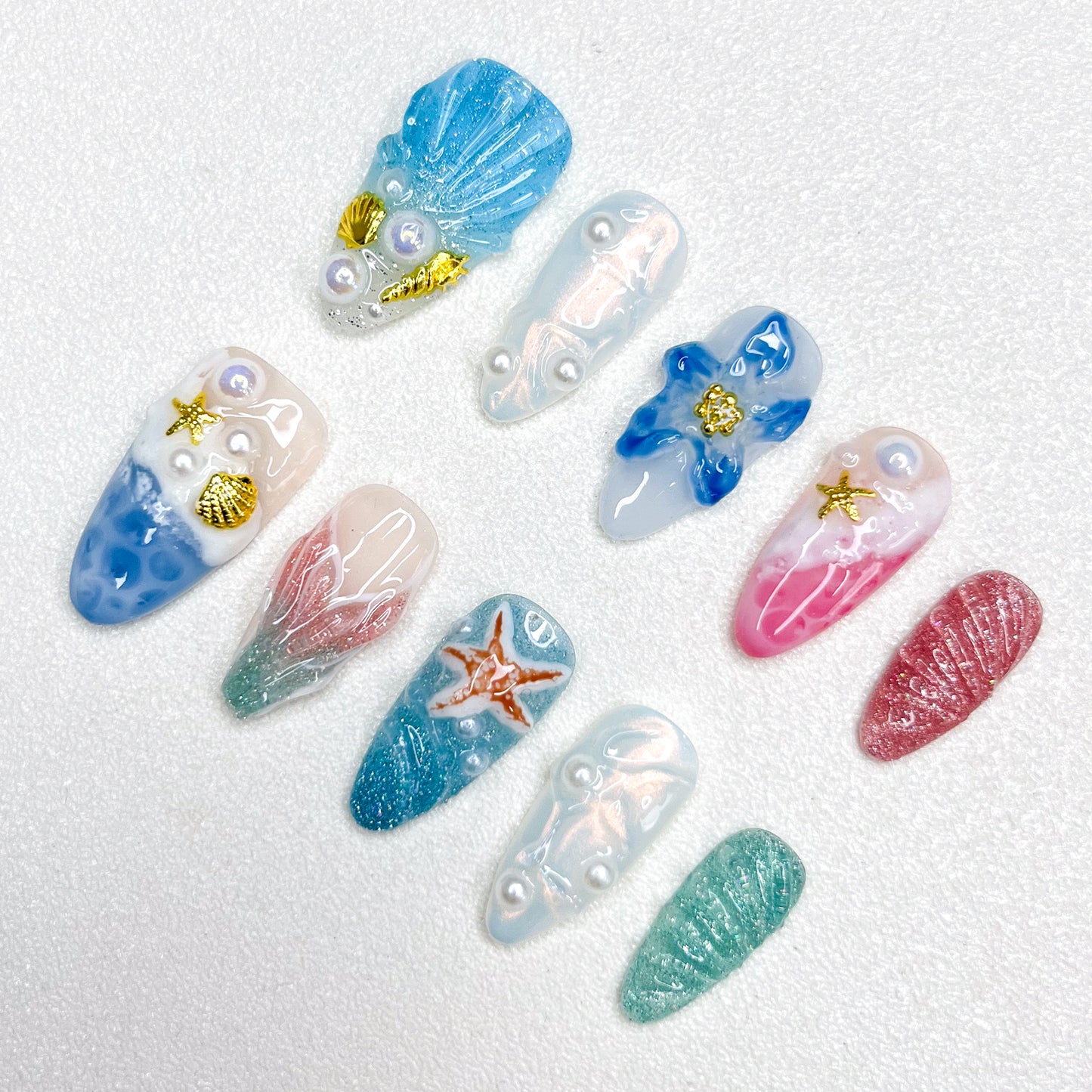 Mermaid-inspired press-on nails with blue and pink gradients, seashell textures, 3D pearls, gold seashell charms, and oceanic elements for dreamy undersea aesthetics.
