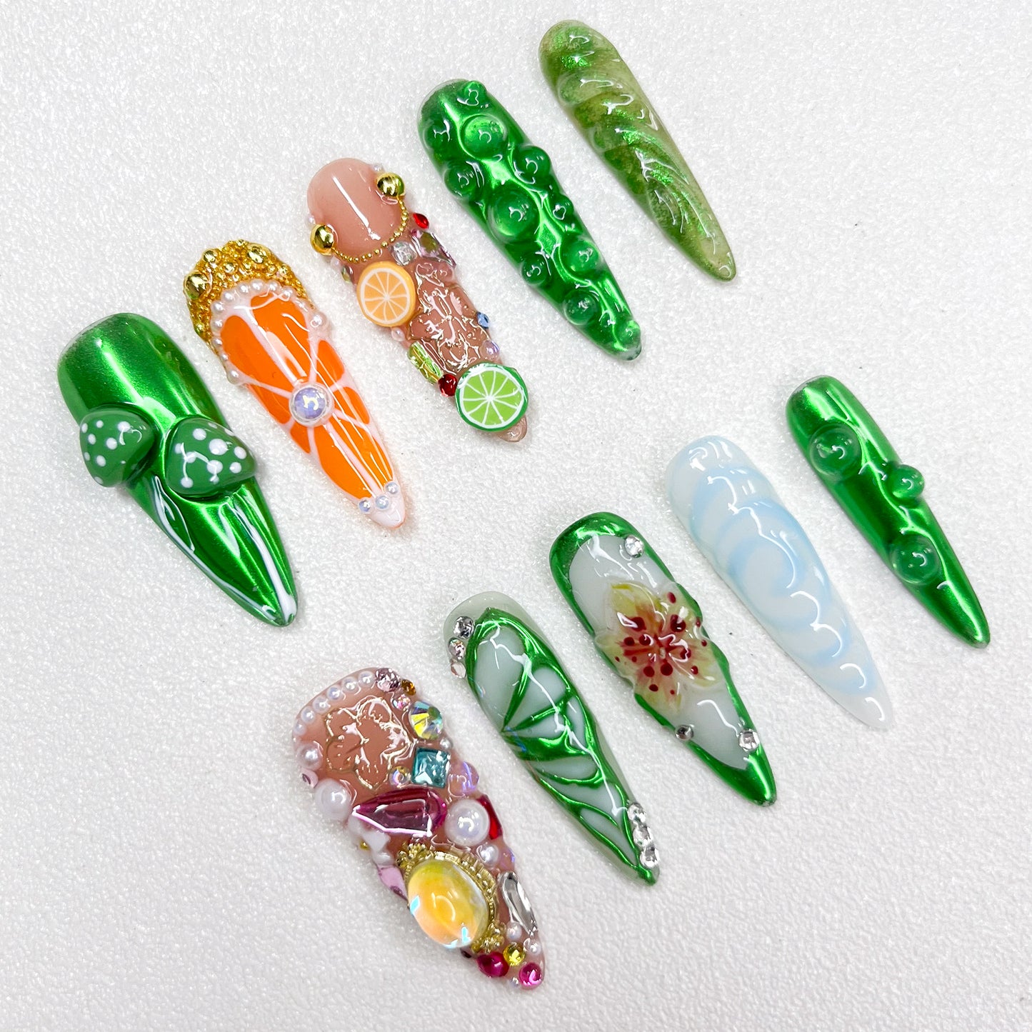 A vibrant nature-inspired press-on nail set with glossy green finishes, mushrooms, citrus fruits, flower petals, and gemstone embellishments, resembling a fantasy garden or enchanted forest.