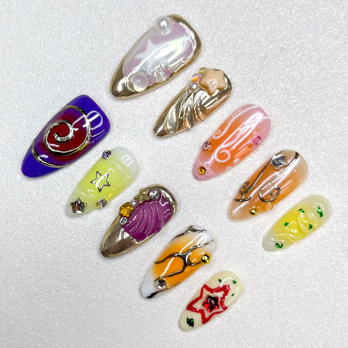 Galaxy-inspired press-on nails with star motifs, music notes, swirl designs, and metallic accents. Features shades of purple, gold, yellow, and orange, blended with celestial themes and 3D embellishments.