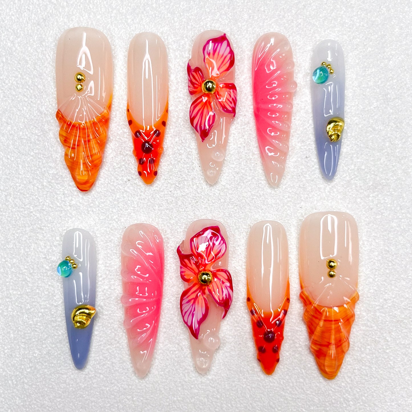 Press-on nails with fiery orange and pink flame tips, vivid hibiscus flower accents, soft gradient backgrounds, and gold studs. Featuring 3D floral textures and translucent jelly finishes, evoking tropical sunsets and vibrant blooms.