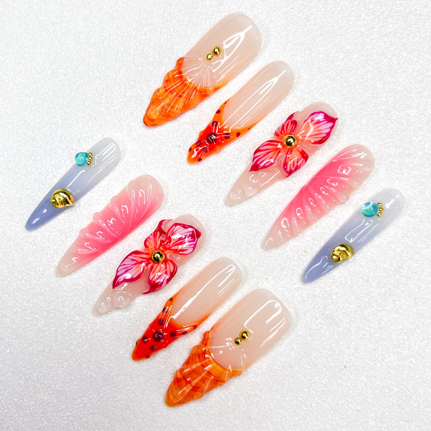Press-on nails with fiery orange and pink flame tips, vivid hibiscus flower accents, soft gradient backgrounds, and gold studs. Featuring 3D floral textures and translucent jelly finishes, evoking tropical sunsets and vibrant blooms.