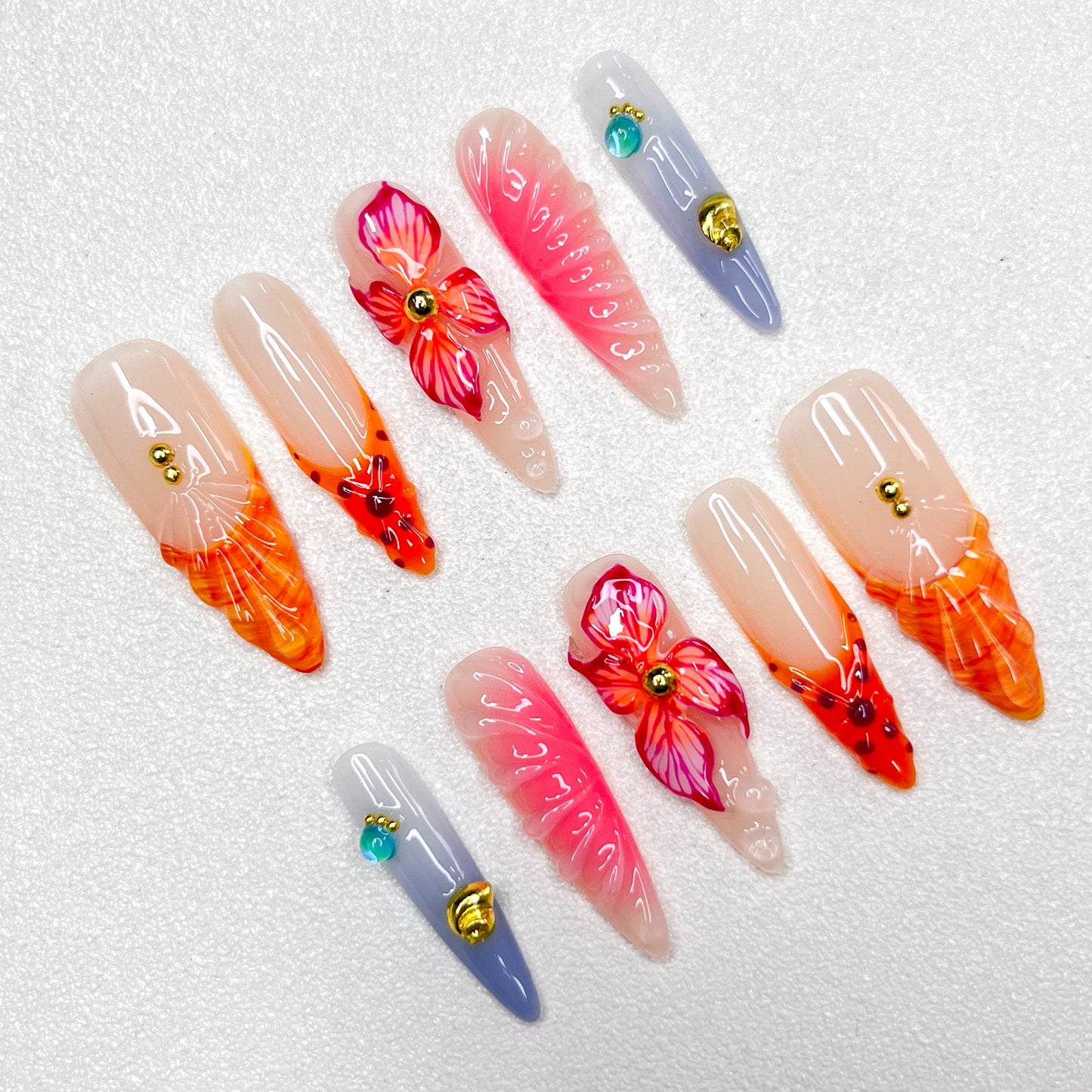 Press-on nails with fiery orange and pink flame tips, vivid hibiscus flower accents, soft gradient backgrounds, and gold studs. Featuring 3D floral textures and translucent jelly finishes, evoking tropical sunsets and vibrant blooms.