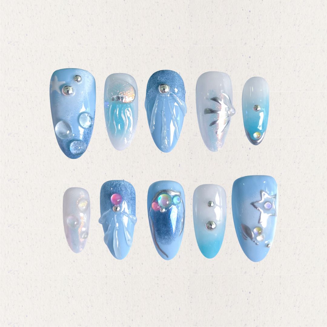 A set of press - on nails with light blue tones and intricate underwater designs, including jellyfish, bubbles, and starfish, embellished with shimmering details. The nails have a peaceful and magical look, great for beach trips or summer events.