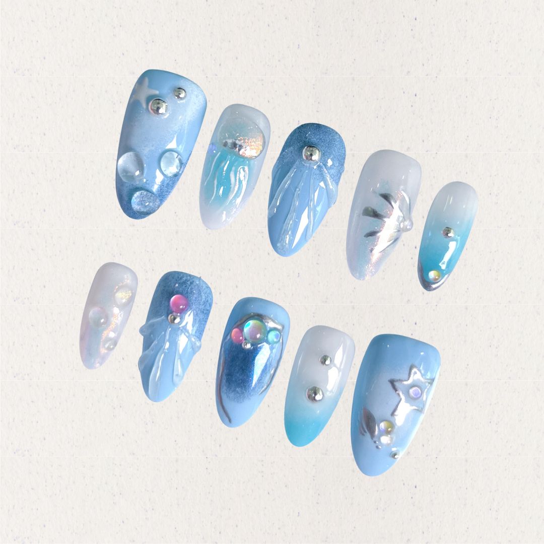 A set of press - on nails with light blue tones and intricate underwater designs, including jellyfish, bubbles, and starfish, embellished with shimmering details. The nails have a peaceful and magical look, great for beach trips or summer events.