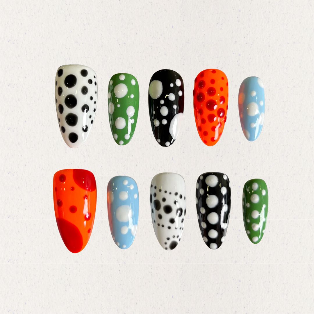 Press-on nails featuring bold polka dot designs in black, white, orange, green, and blue, combining a playful and modern vibe.