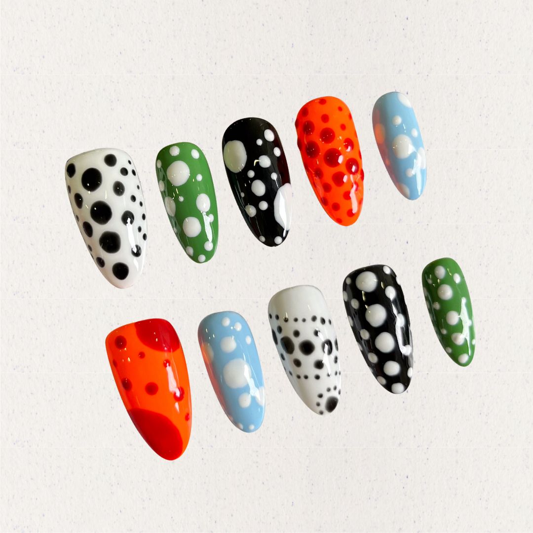 Press-on nails featuring bold polka dot designs in black, white, orange, green, and blue, combining a playful and modern vibe.