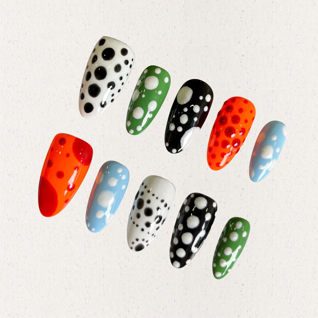 Press-on nails featuring bold polka dot designs in black, white, orange, green, and blue, combining a playful and modern vibe.