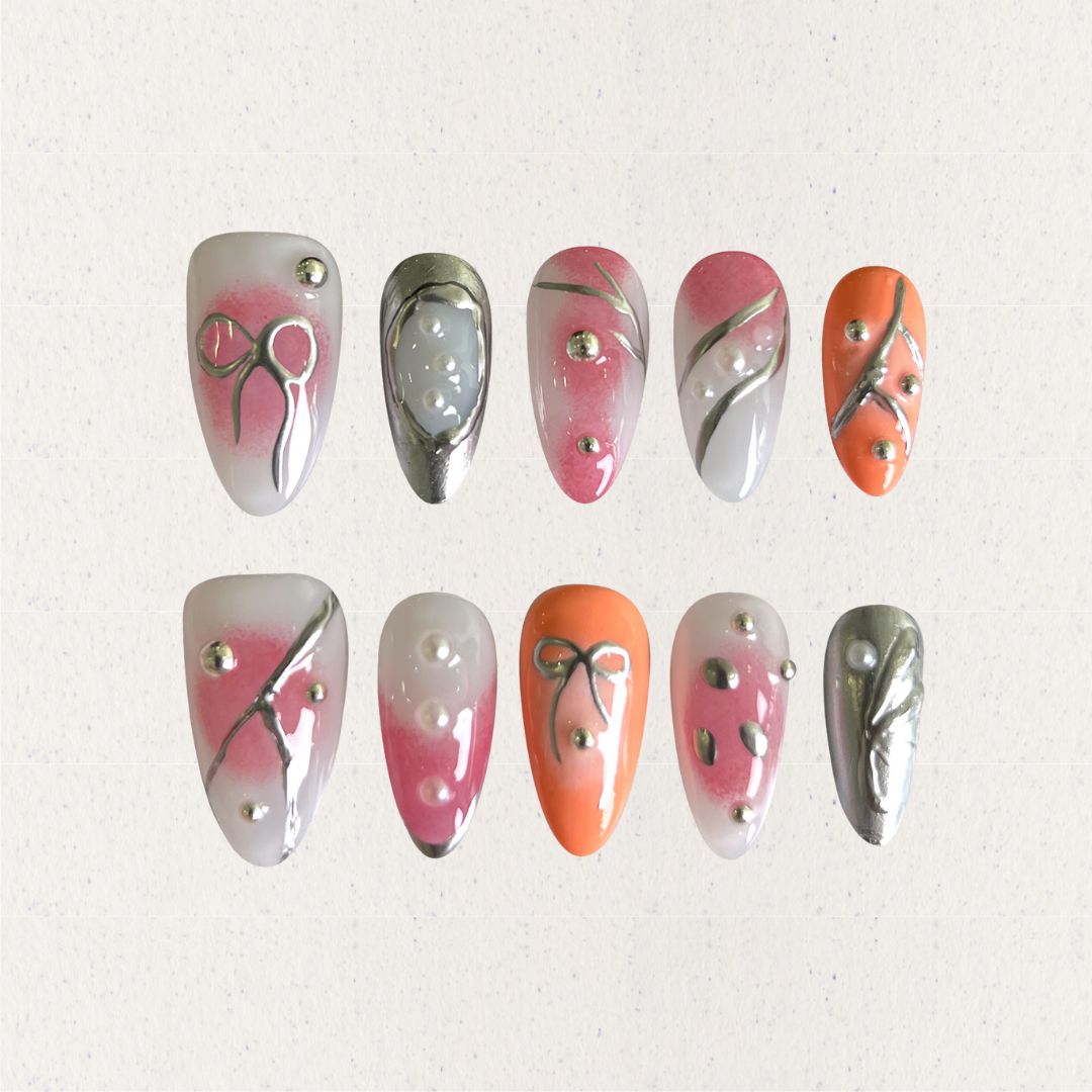 Press-on nails featuring delicate bows, metallic silver lines, and soft pink-to-orange gradients for a classy and sophisticated look.