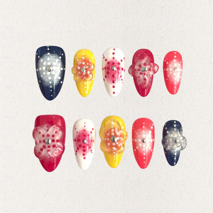 Bright press-on nails with dotted floral designs and translucent petals in warm, cheerful colors.