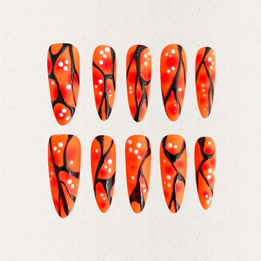 Orange and black press-on nails with coral-like patterns and white dot accents, delivering a natural and artistic appeal.