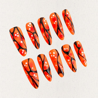 Orange and black press-on nails with coral-like patterns and white dot accents, delivering a natural and artistic appeal.