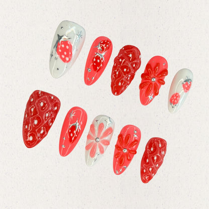 Elegant press-on nails inspired by strawberries, showcasing vibrant red textures and delicate white highlights for a charming touch.