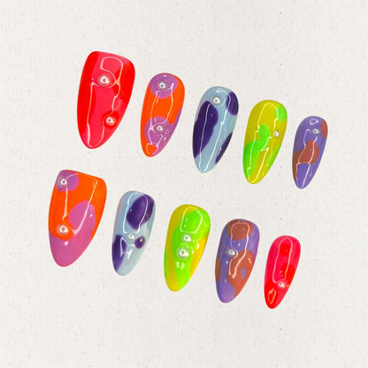 Colorful press-on nails with neon abstract patterns, featuring playful dots and fluid shapes in vivid hues.