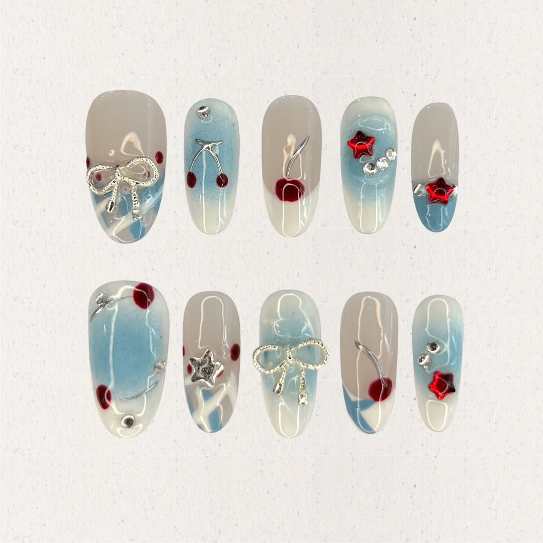 Elegant press-on nails with soft blue gradients, silver bows, and vibrant cherry accents, creating a balanced mix of refinement and playful charm.