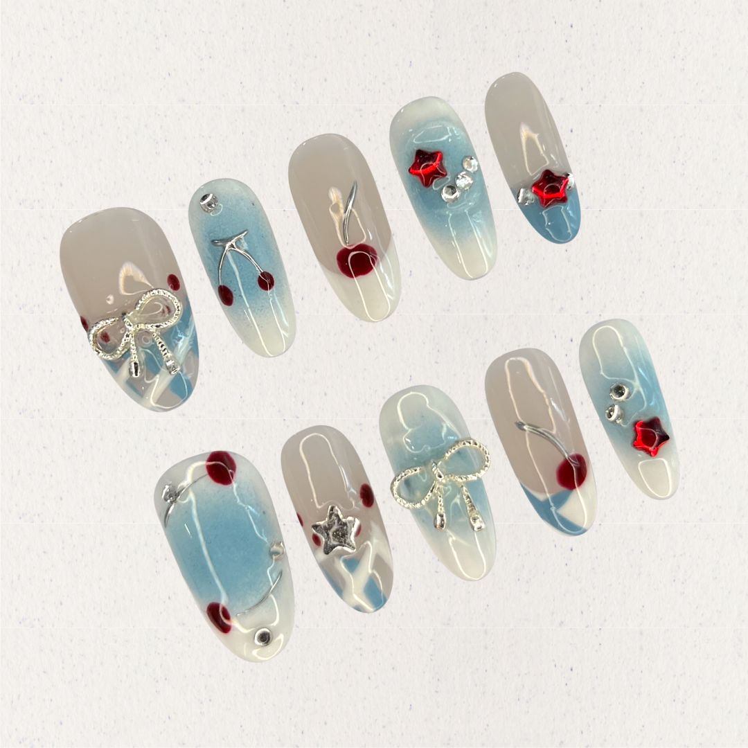 Elegant press-on nails with soft blue gradients, silver bows, and vibrant cherry accents, creating a balanced mix of refinement and playful charm.