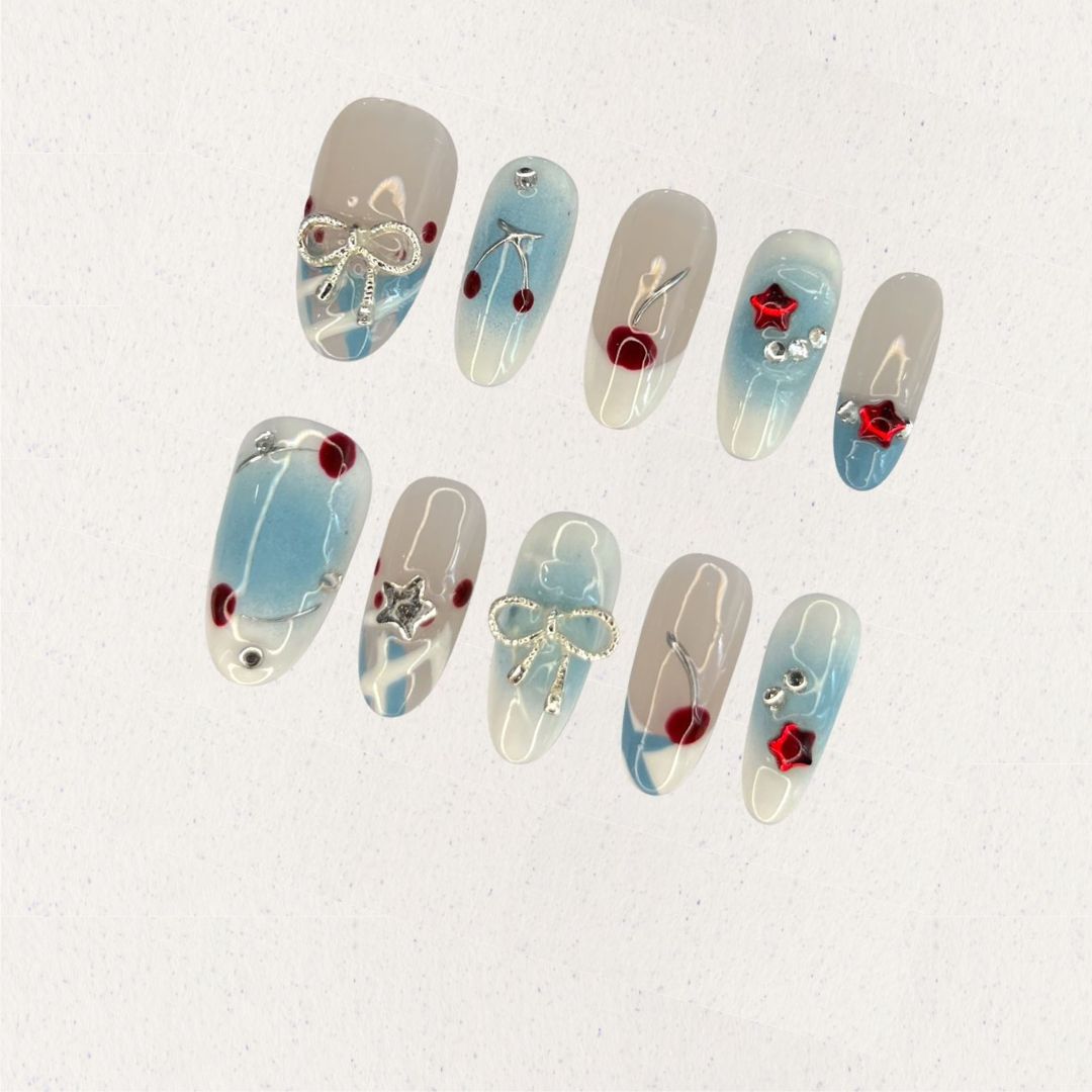 Elegant press-on nails with soft blue gradients, silver bows, and vibrant cherry accents, creating a balanced mix of refinement and playful charm.