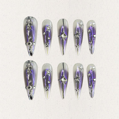 Celestial Radiance presents gradient silver and purple press-on nails with metallic embellishments, including stars and crosses, evoking a celestial and sophisticated style.