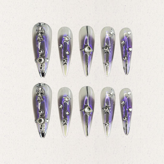 Celestial Radiance presents gradient silver and purple press-on nails with metallic embellishments, including stars and crosses, evoking a celestial and sophisticated style.