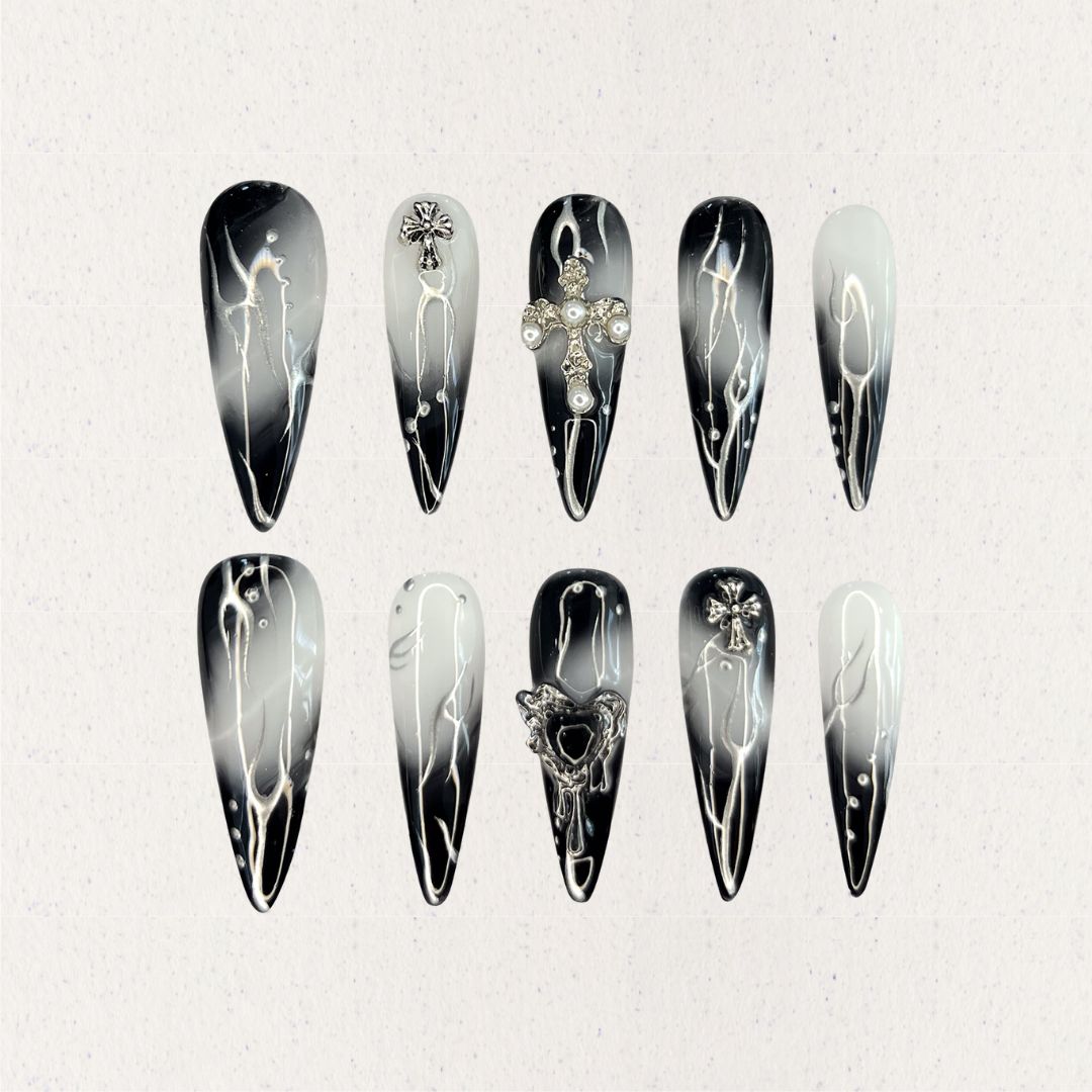 Gothic Veil showcases gradient black and white nails adorned with metallic cross embellishments and pearl details, reflecting a gothic and elegant aesthetic.