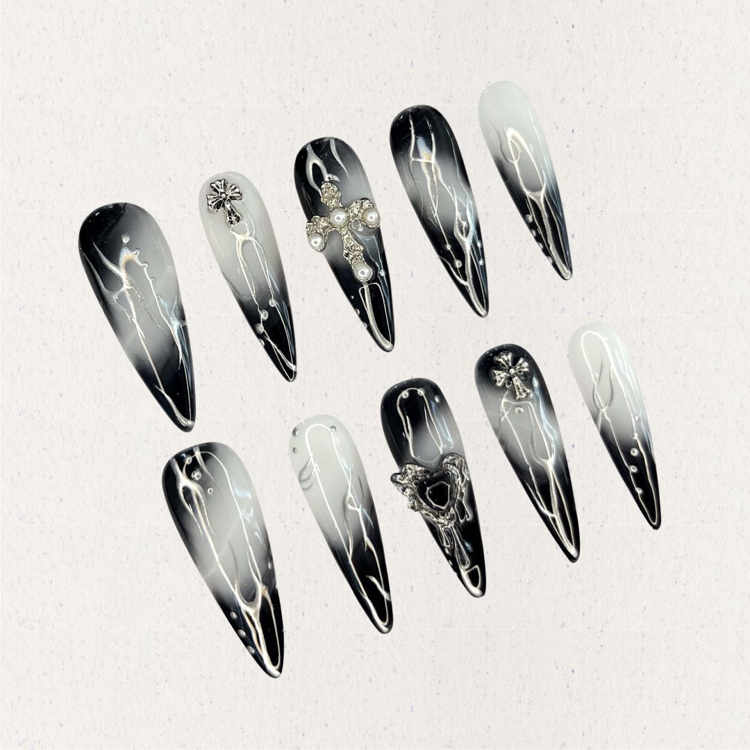 Gothic Veil showcases gradient black and white nails adorned with metallic cross embellishments and pearl details, reflecting a gothic and elegant aesthetic.