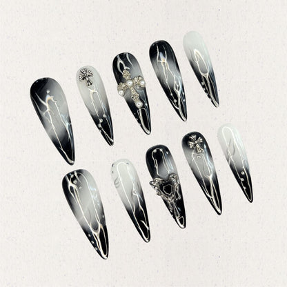 Gothic Veil showcases gradient black and white nails adorned with metallic cross embellishments and pearl details, reflecting a gothic and elegant aesthetic.