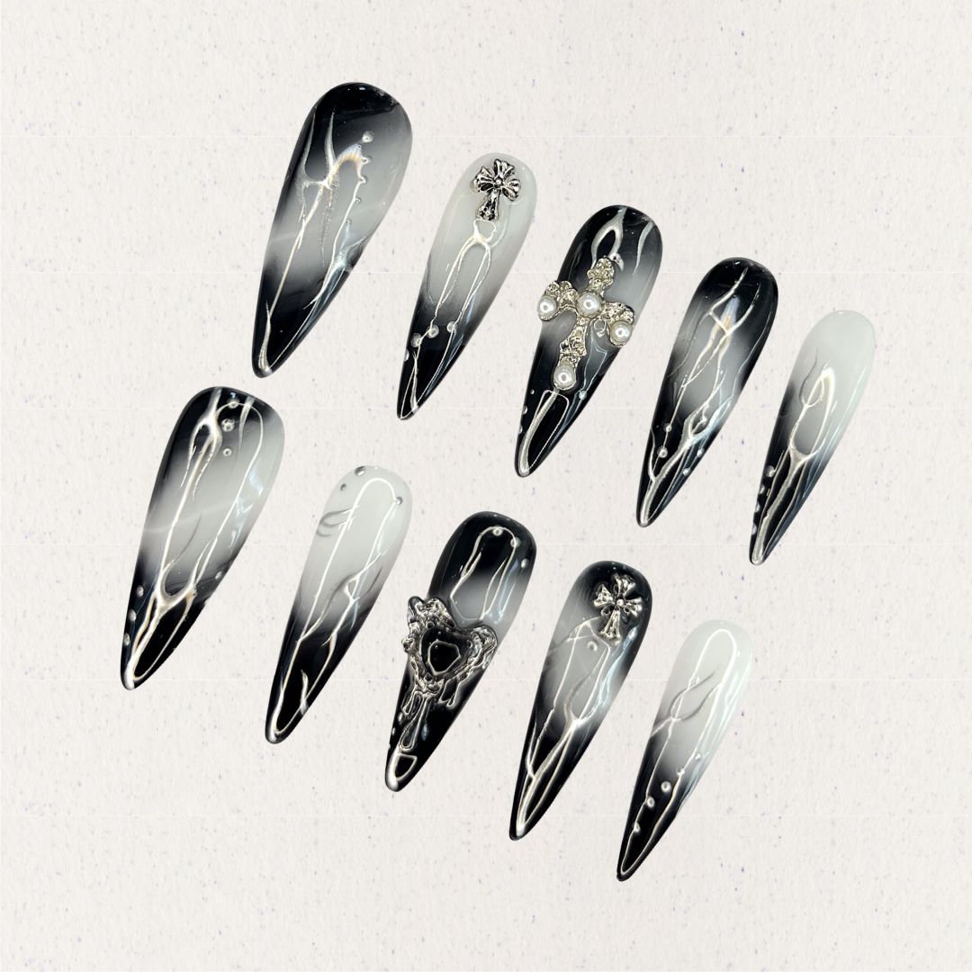 Gothic Veil showcases gradient black and white nails adorned with metallic cross embellishments and pearl details, reflecting a gothic and elegant aesthetic.