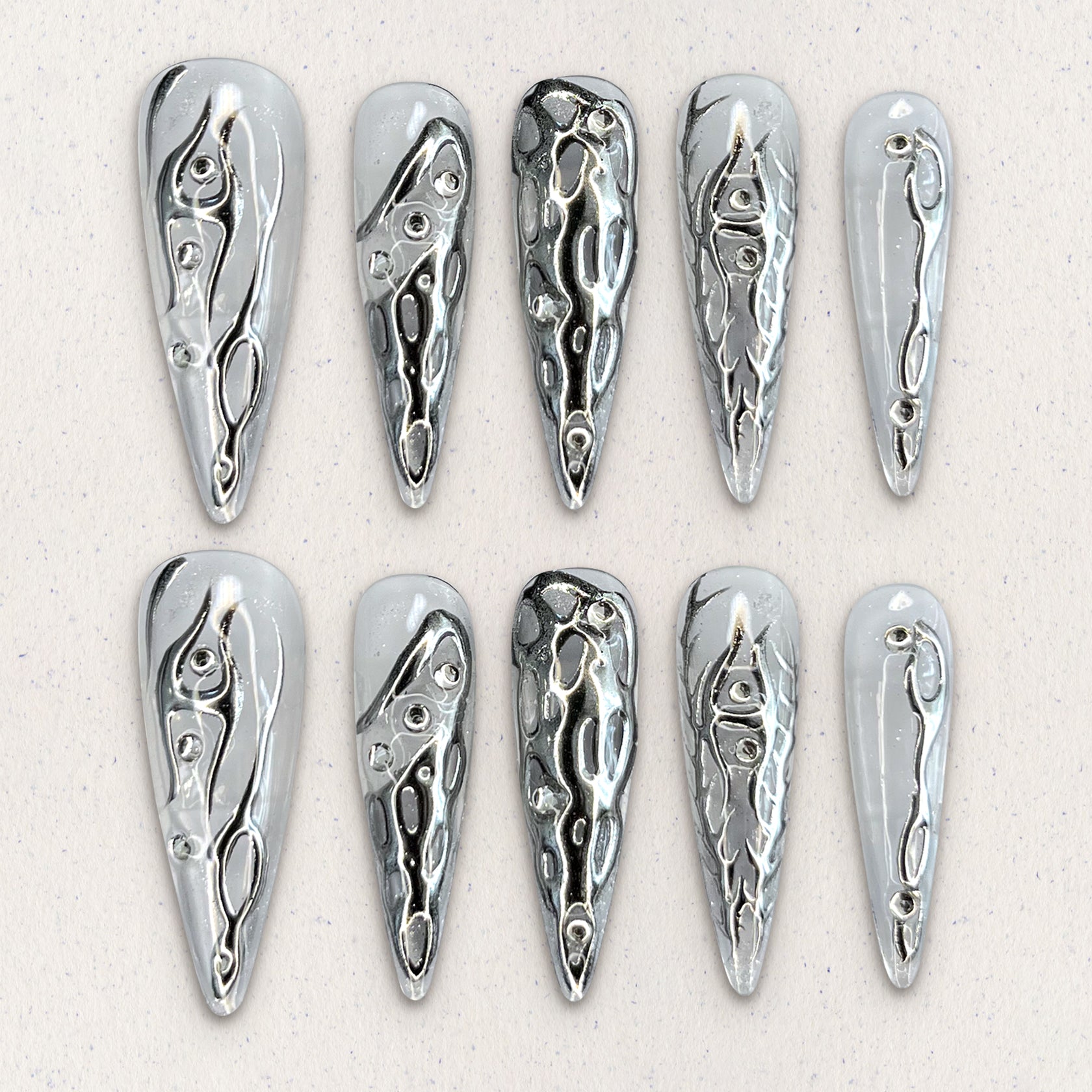 Liquid Metal Elegance features reflective silver press-on nails with flowing metallic patterns, creating a contemporary and bold aesthetic.