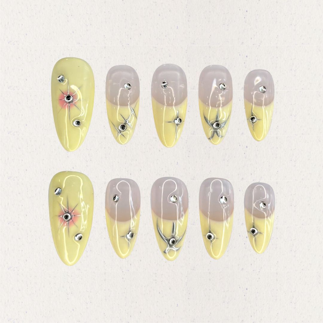 Lemon Gleam press-on nails with a soft gradient of yellow and nude shades, decorated with intricate silver linework and radiant starburst details, adding a touch of elegance and charm to your style.