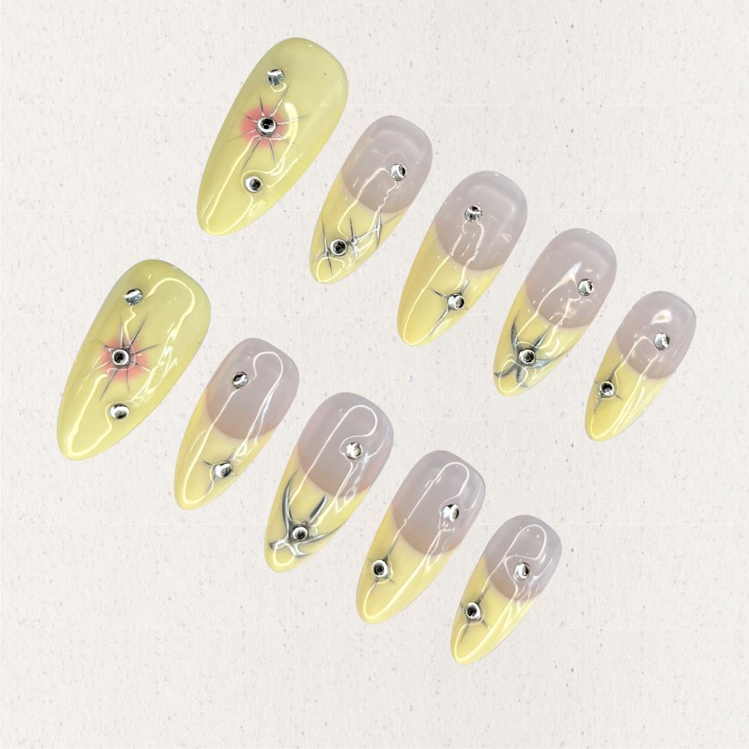 Lemon Gleam press-on nails with a soft gradient of yellow and nude shades, decorated with intricate silver linework and radiant starburst details, adding a touch of elegance and charm to your style.