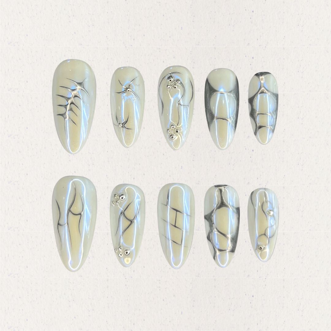 Fossil Radiance nail set features metallic pale shades with skeletal textures, geometric lines, and subtle shimmering accents, creating a sophisticated and enigmatic aesthetic.