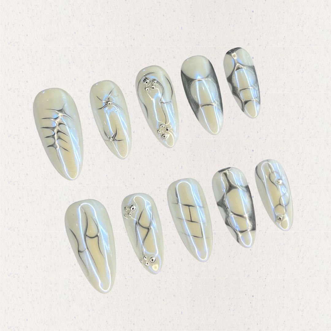 Fossil Radiance nail set features metallic pale shades with skeletal textures, geometric lines, and subtle shimmering accents, creating a sophisticated and enigmatic aesthetic.