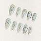 Fossil Radiance nail set features metallic pale shades with skeletal textures, geometric lines, and subtle shimmering accents, creating a sophisticated and enigmatic aesthetic.