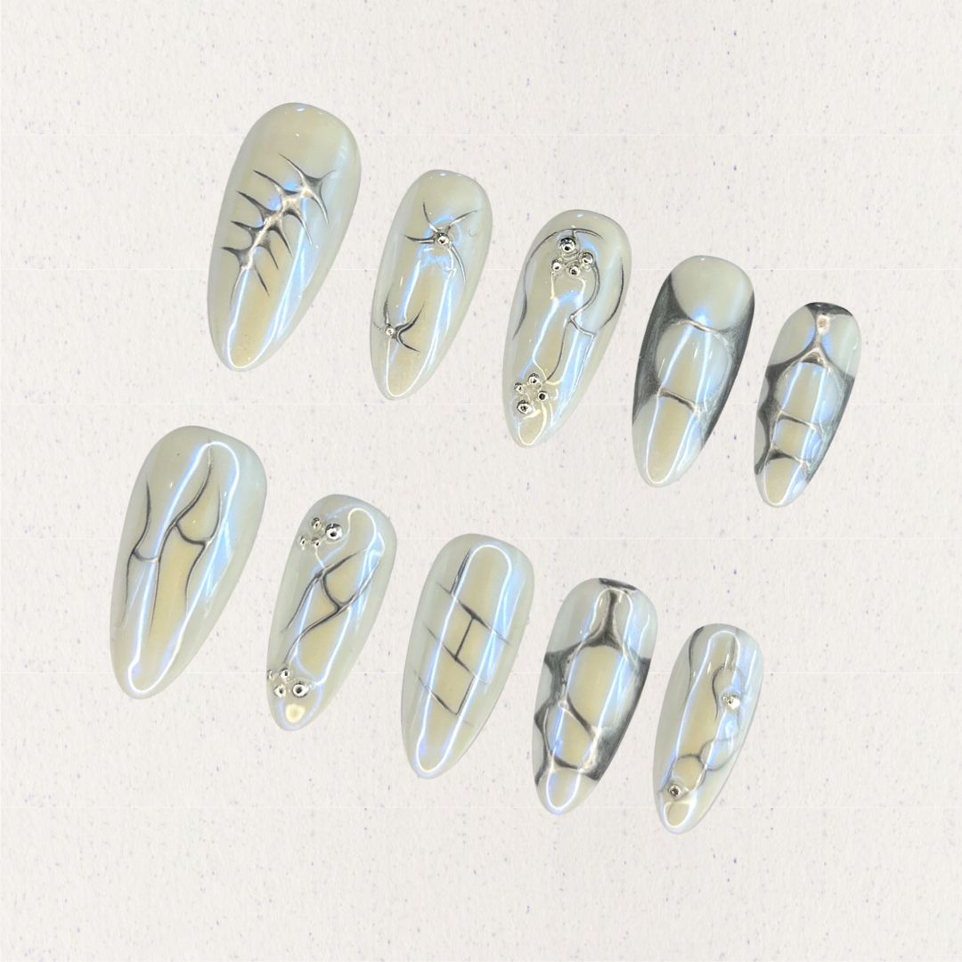 Fossil Radiance nail set features metallic pale shades with skeletal textures, geometric lines, and subtle shimmering accents, creating a sophisticated and enigmatic aesthetic.