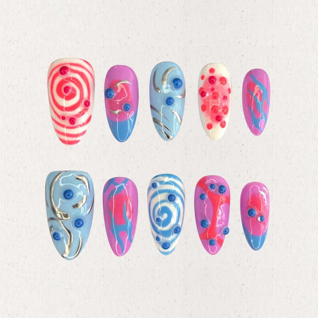 Cosmic Swirls nail set features bold swirls of pink, blue, and white, accented with metallic details and circular 3D elements. This playful yet elegant design mirrors the energetic flow of cosmic waves and nebulae.