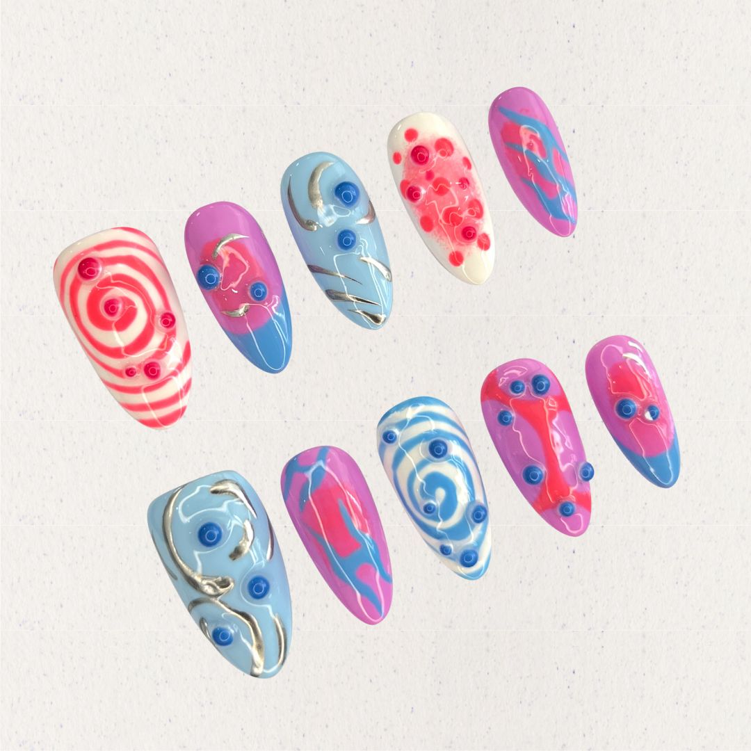 Cosmic Swirls nail set features bold swirls of pink, blue, and white, accented with metallic details and circular 3D elements. This playful yet elegant design mirrors the energetic flow of cosmic waves and nebulae.